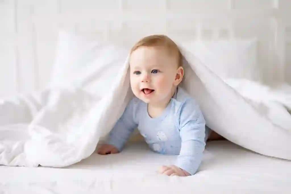 Kichkina sog'lom chaqaloq uyda yotibdi oq choyshab ko'k tana kiyimi baxtli chaqaloq oshqozonida yotgan to'qimachilik choyshablari bolalar | Small healthy baby is lying home blanket white bed linen blue bodysuit happy baby lying his stomach textiles bedding children