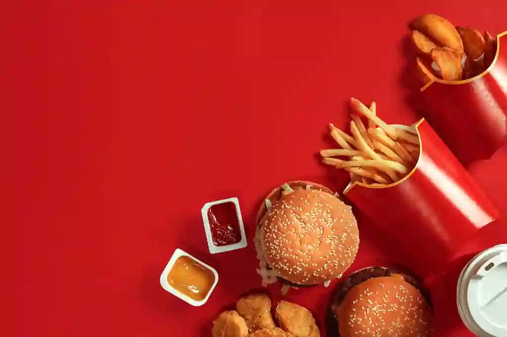 Fast tamaddi qilishga mo'ljallangan taom, go'shtli burger kartoshka chiplari, shisha ichimlik qizil fonida | Fast food dish top view meat burger potato chips glass drink red background takeaway compo