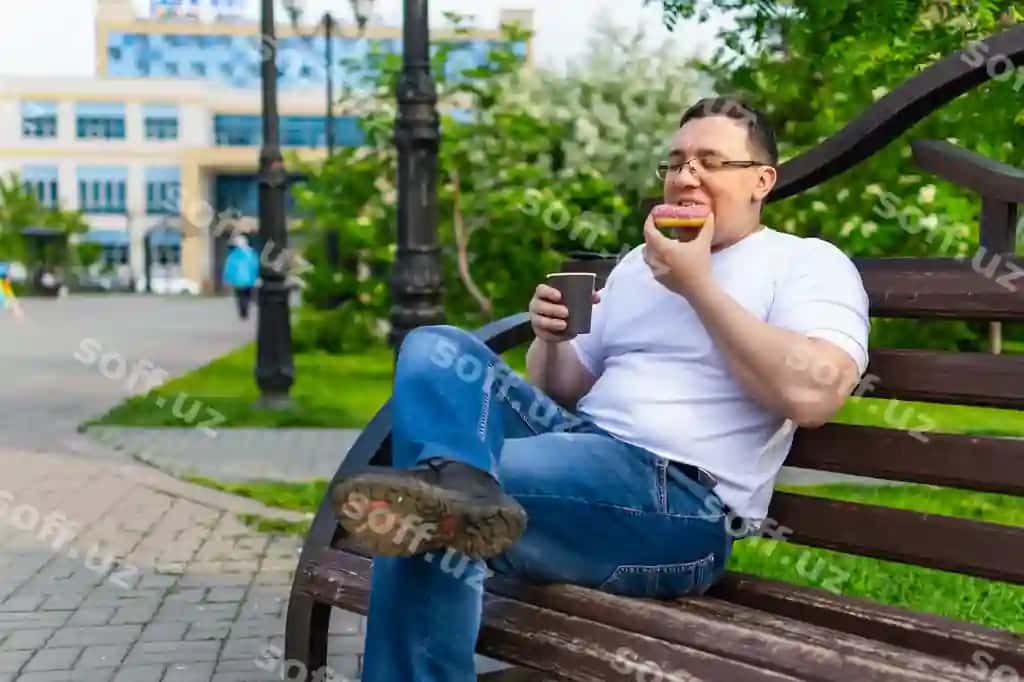 Erkak yozda parkdagi taxtakda o'tirib donutni hisobga olayotgan. | Man enjoying donut while sitting park bench summer