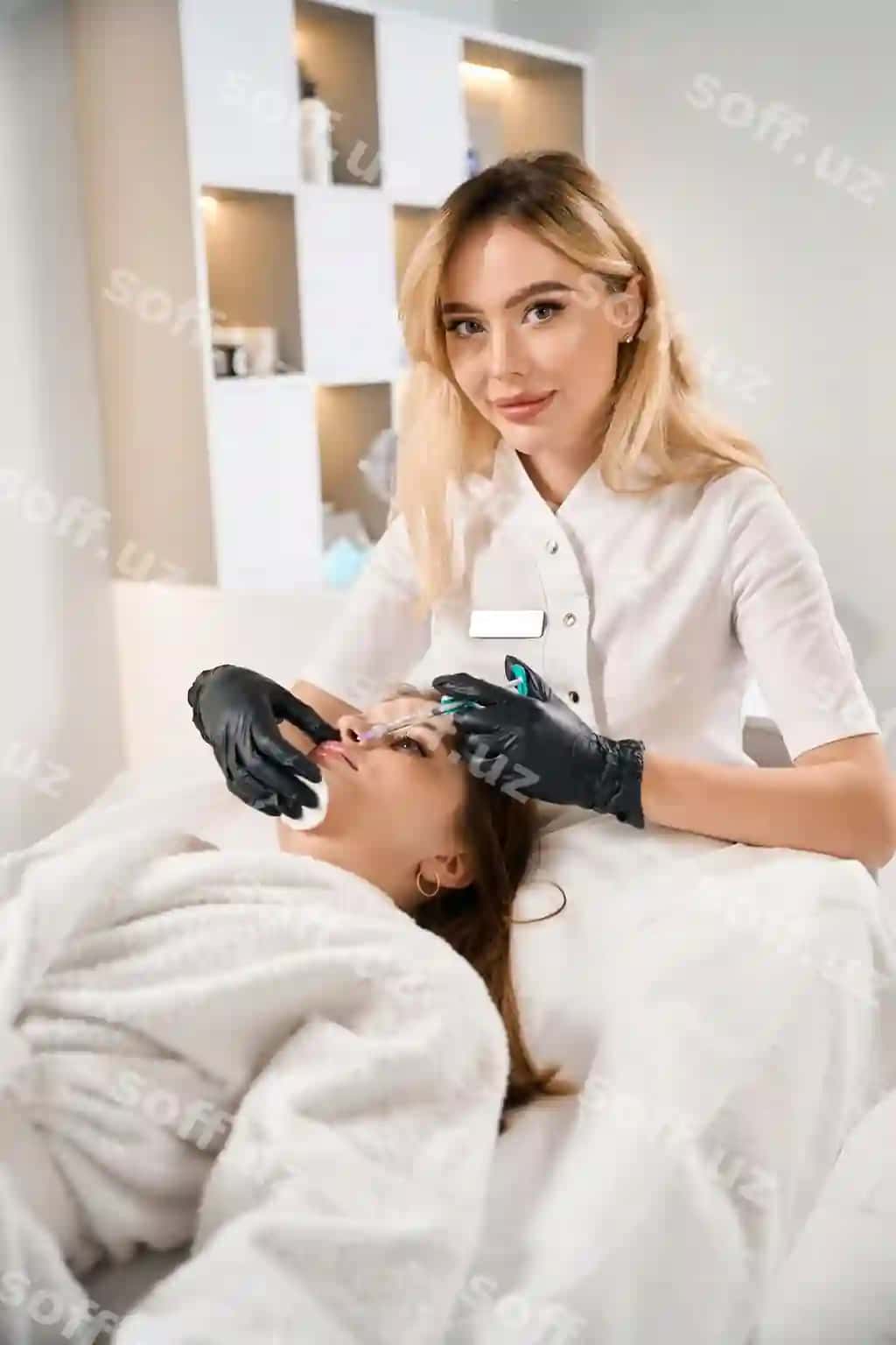 Ayol beauty terapisi kameraga qaraydi, ayolning lablariga beauty injeksiyasi bajarayotganda. | Female beautician looking camera while doing lips beauty injection woman